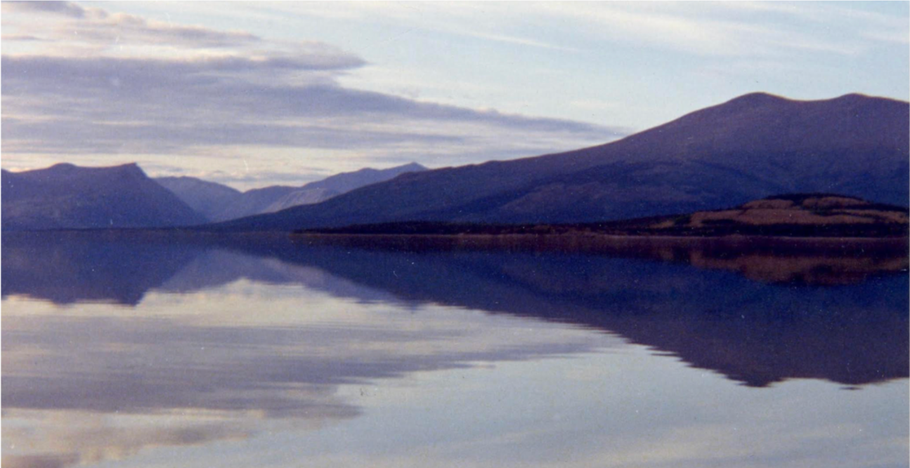 Still lake at dusk mirroring a range of blue mountains and soft cloud